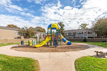 A playground with a yellow and blue slide in the middle of a grassy area.